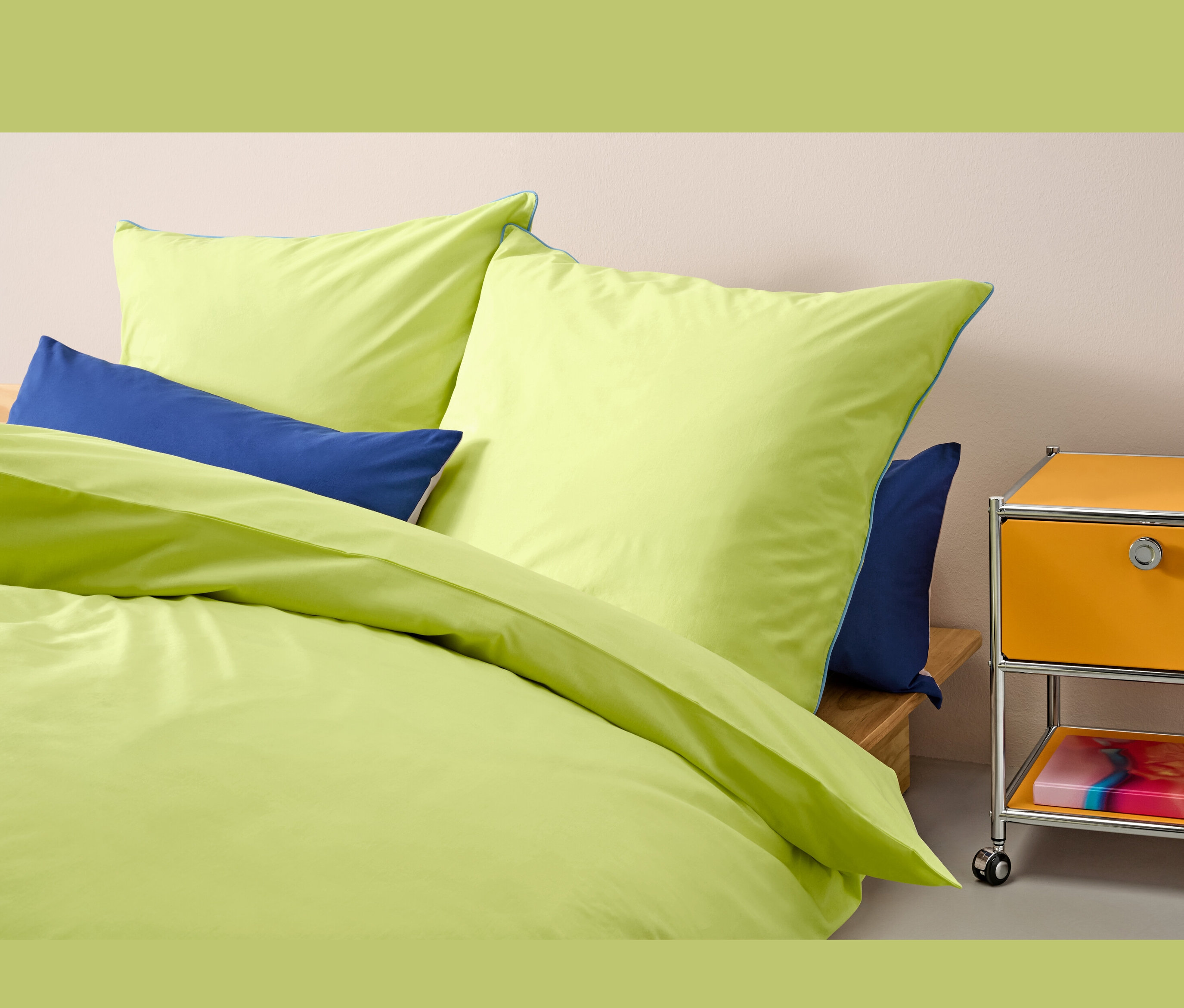 Světle zelené povlečení renforcé standardní velikosti na posteli s modrými polštáři.