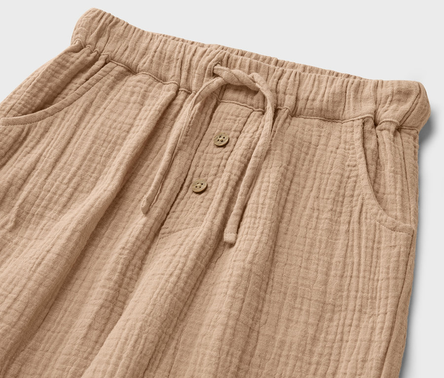 Detail dětských mušelínových kalhot se stahovací šňůrkou a knoflíky.