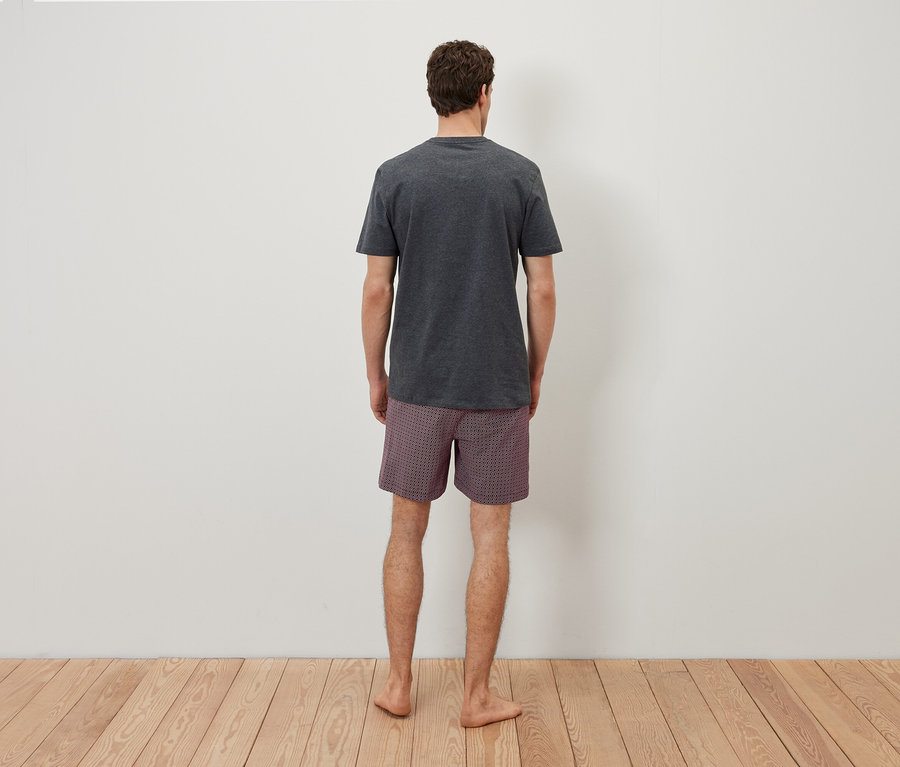 Muž zády ke kameře má na sobě šedé tričko a kostkované šortky.
