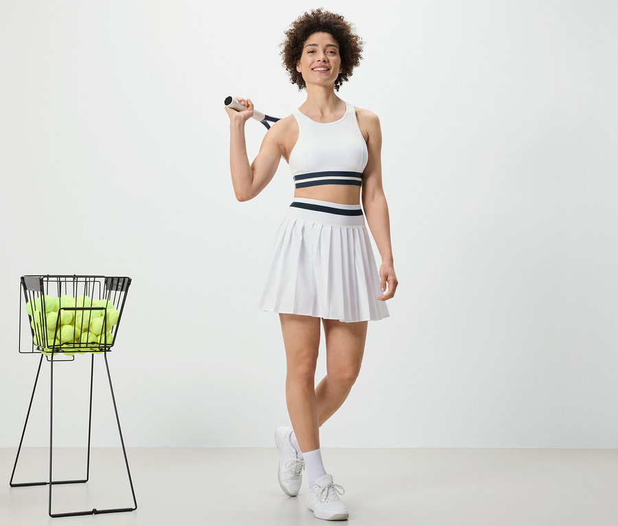 Žena drží tenisovou raketu a má na sobě sportovní sukni.