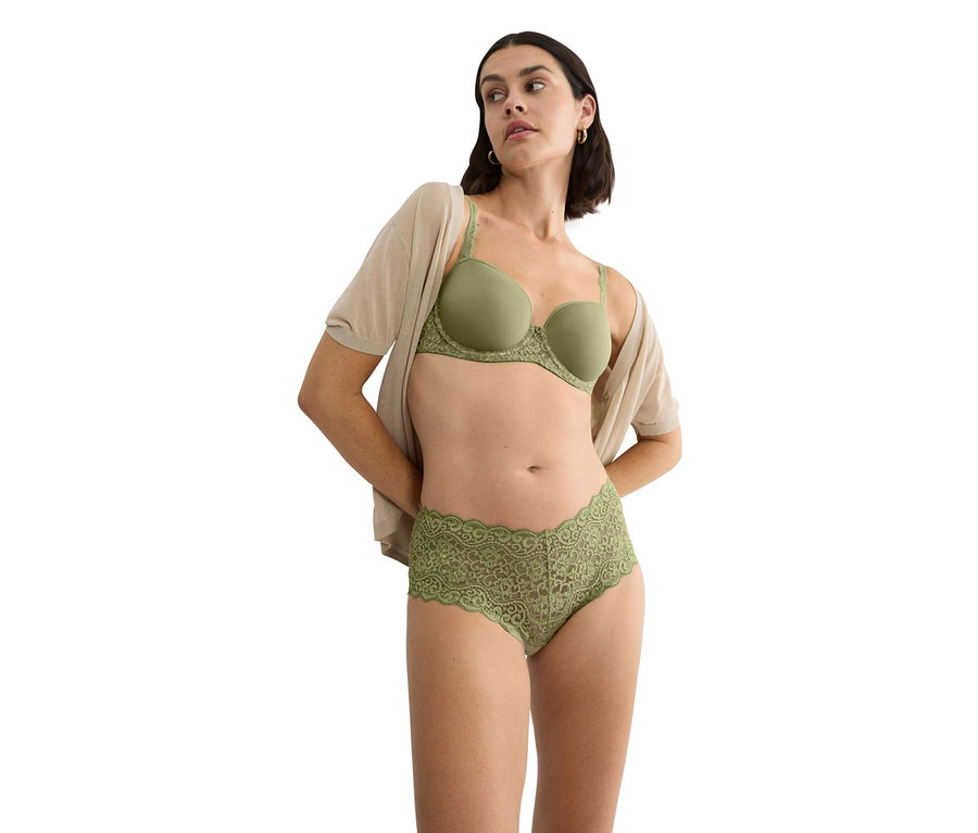 Žena má na sobě zelenou podprsenku s krajkovým lemem a odpovídající krajkové kalhotky a béžový kardigan.
