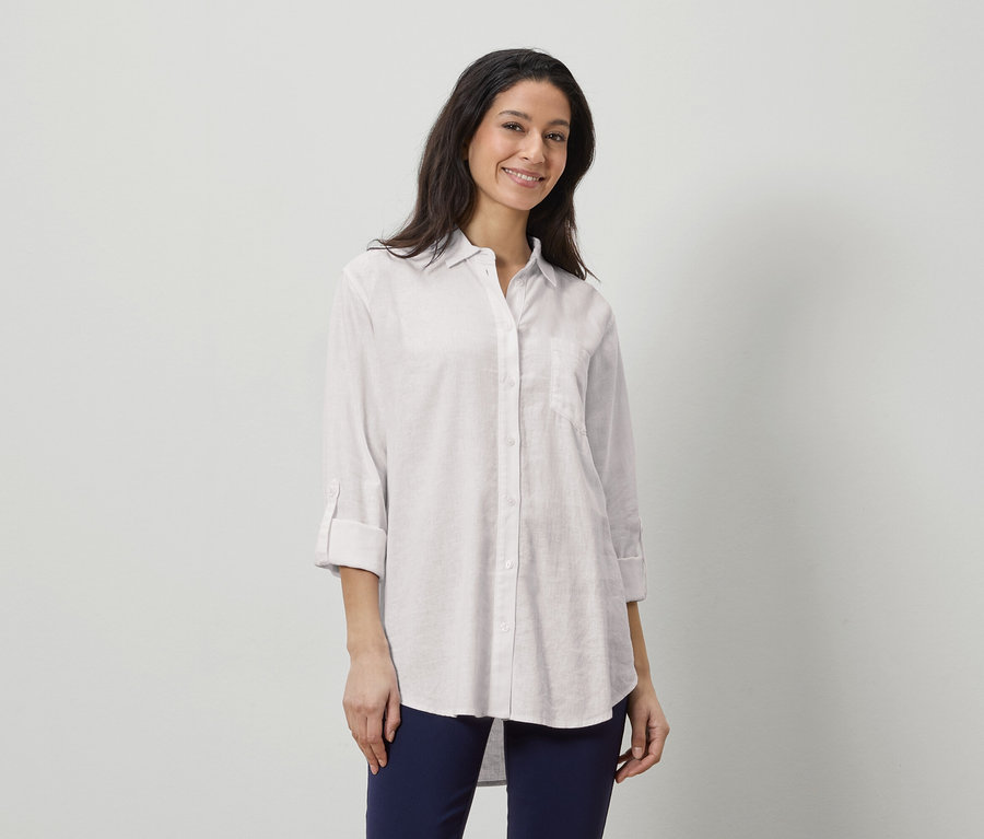 Žena má na sobě bílou lněnou košili a tmavě modré kalhoty.