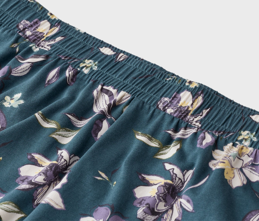 Detailní záběr na modré pyžamové kalhoty s elastickým pasem a květinovým vzorem.