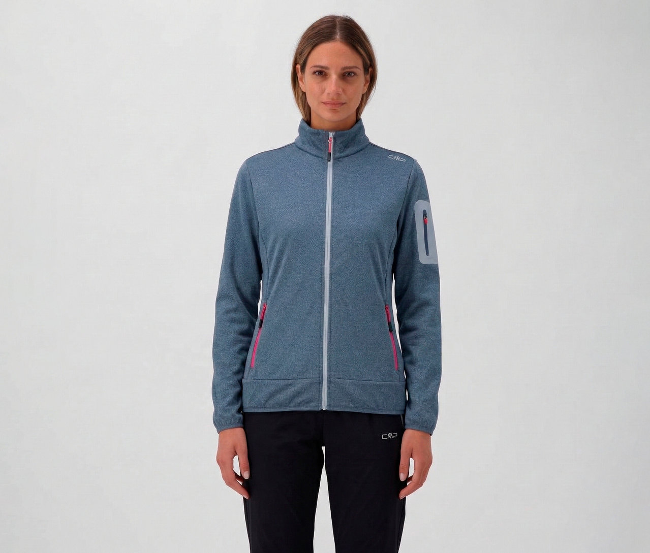 Žena má na sobě modrou melírovanou dámskou bundu CMP s celopropínacím zipem a černé kalhoty na neutrálním pozadí.
