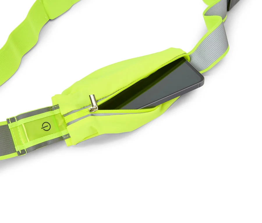 Neonově žlutý běžecký pás s kapsou na zip, ve které je zasunutý smartphone. Na reflexním proužku je vidět symbol vypínače.