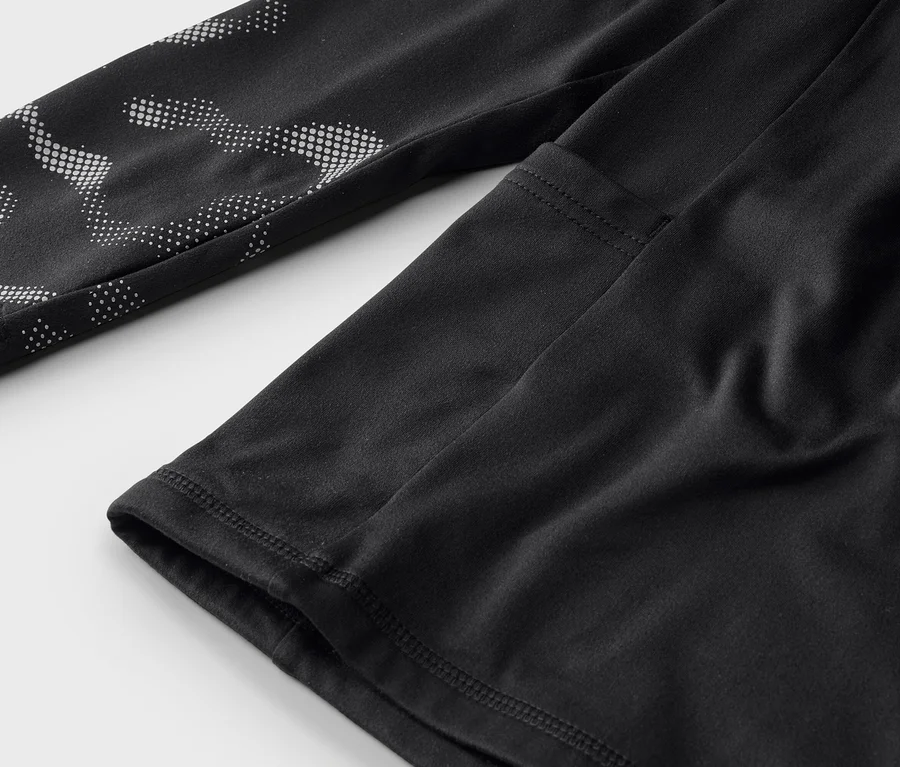 Detailní záběr na černé sportovní tričko s dlouhým rukávem a bílým tečkovaným vzorem na rukávu.