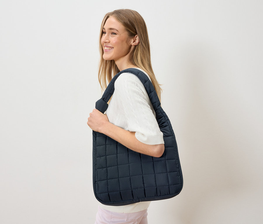 Žena nosí přes rameno tmavě modrou, prošívanou tašku.