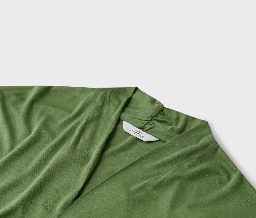 Detail zeleného zavinovacího topu s výstřihem do V a štítkem s nápisem „TCHIRO MY STYLE“.