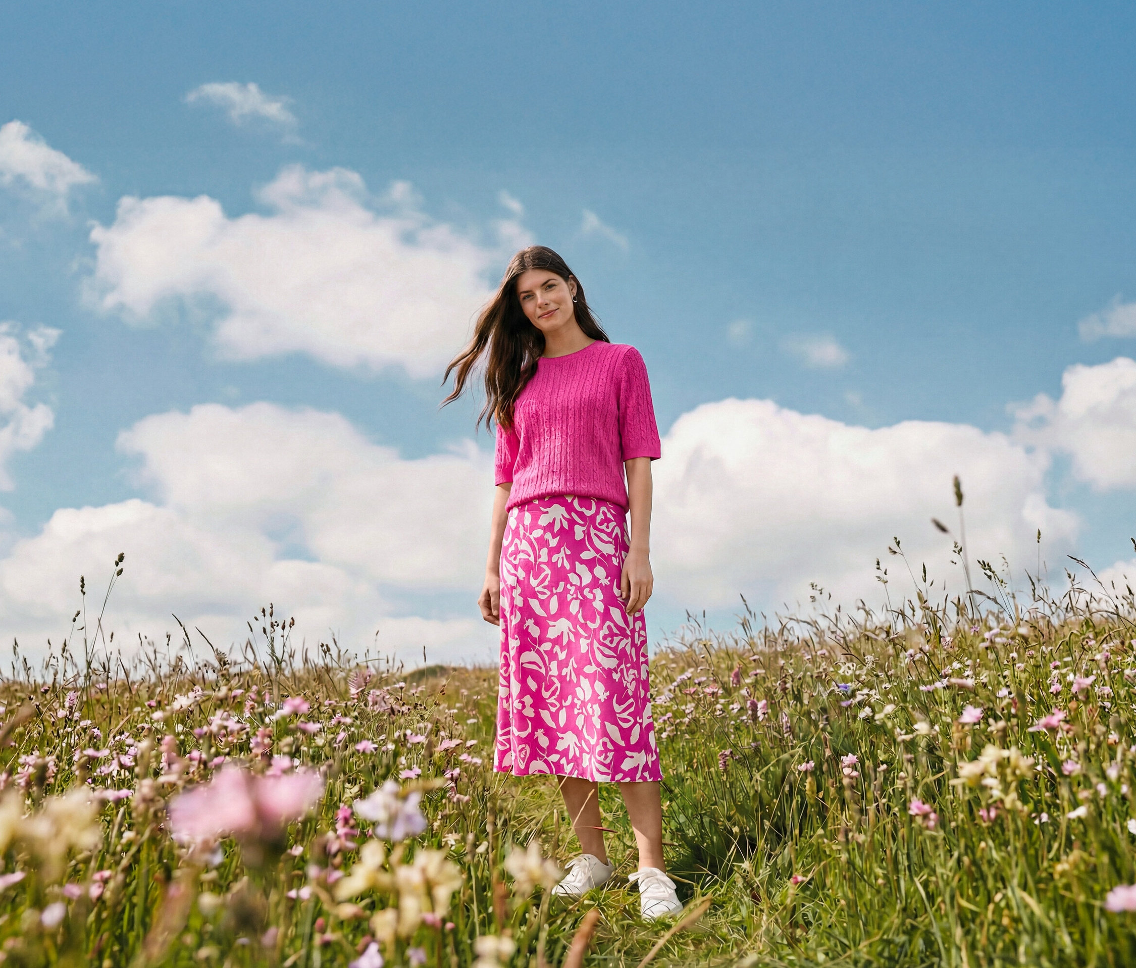 Žena stojí na louce a má na sobě midi sukni s potiskem, náušnice Wave a kožené tenisky.