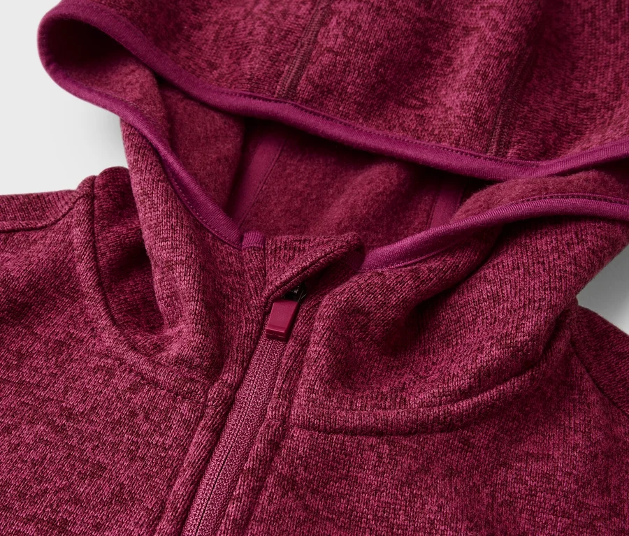 Detail melírované mikiny s kapucí v barvě magenta, se zipem a kapucí lemovanou tmavším magenta páskem.