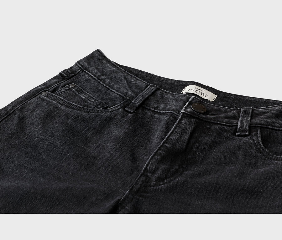 Detail horní části černých džínů, zobrazující přední kapsu, poutka na opasek, tmavý knoflík a bílý štítek „TCHIBO MY STYLE“ na pase.