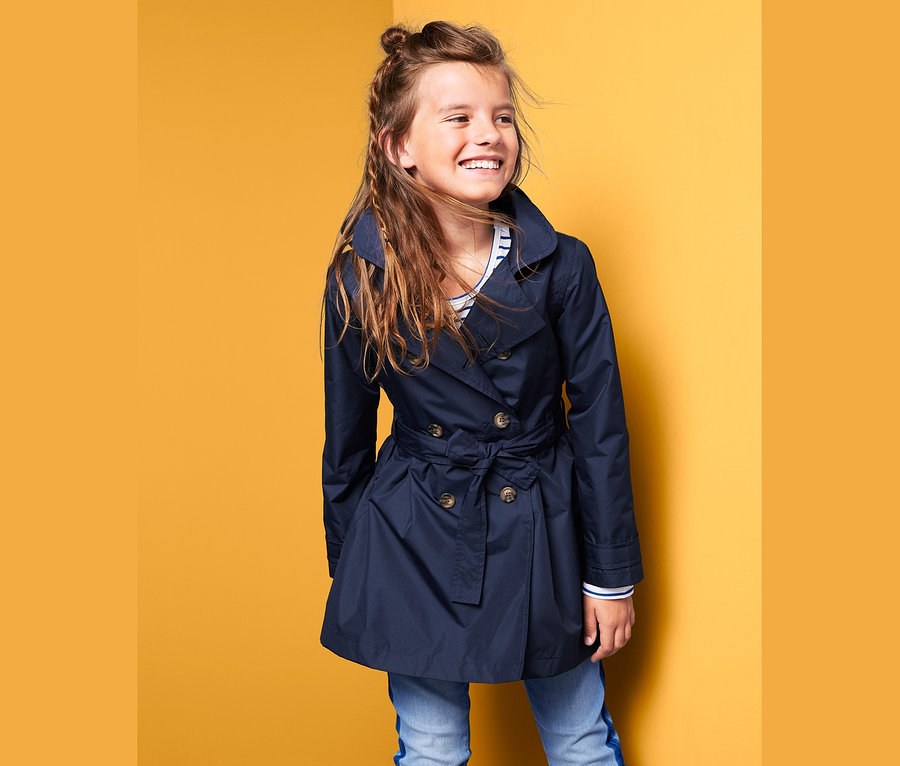 Usmívající se dívka pózuje v tmavě modrém trenčkotu do každého počasí.