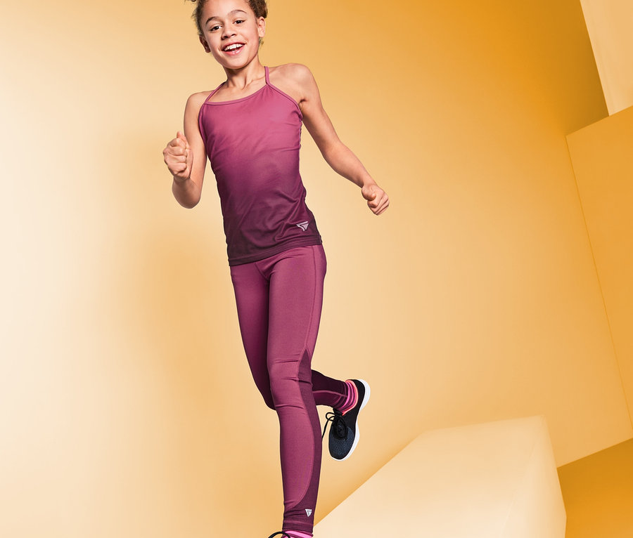 Usmívající se dívka ve sportovních legínách pózuje na žlutém pozadí.
