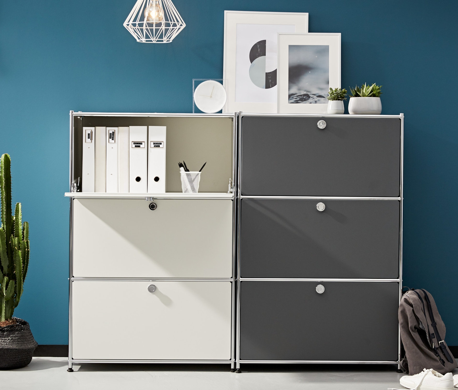 Dva kovové regály se 3 výklopnými dvířky stojí vedle sebe. Jeden je bílý a druhý šedý.