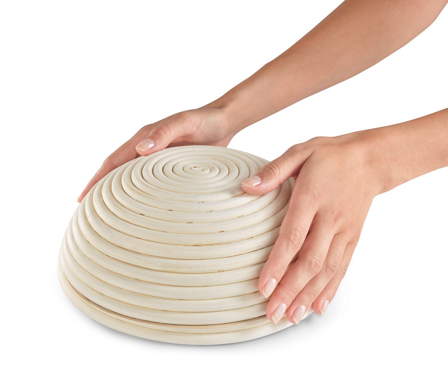 Dvě ruce drží kulatou ošatku na kynutí těsta.