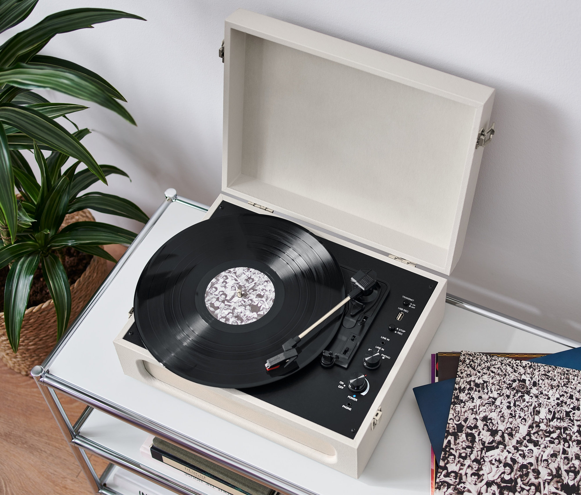 Na bílém stolku stojí otevřený retro gramofon s funkcí Bluetooth® a hraje deska. Vedle leží vinylové desky a v pozadí je vidět rostlina v proutěném košíku.