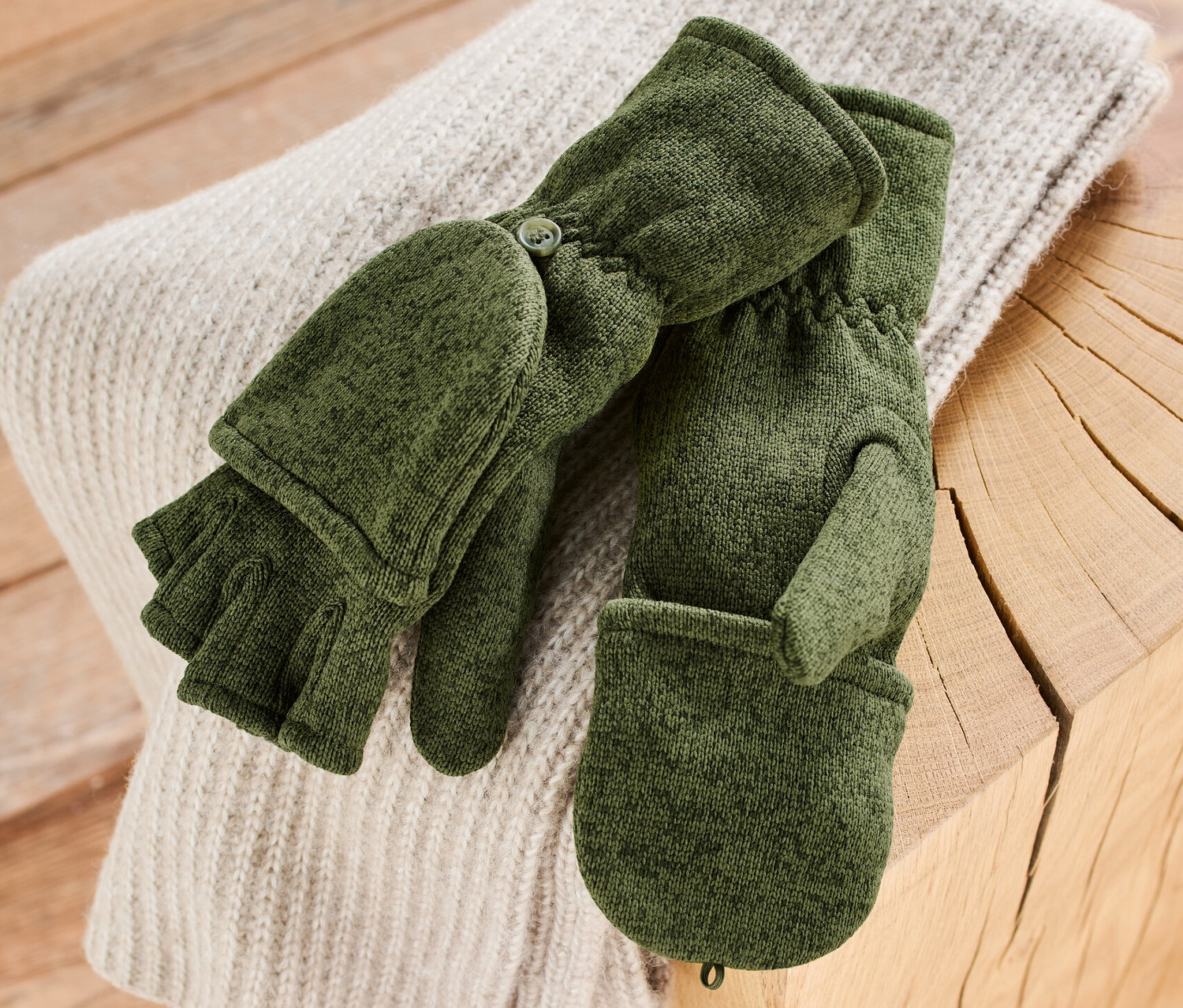 Khaki pletené fleecové palčáky leží na svetru na dřevěném stole.