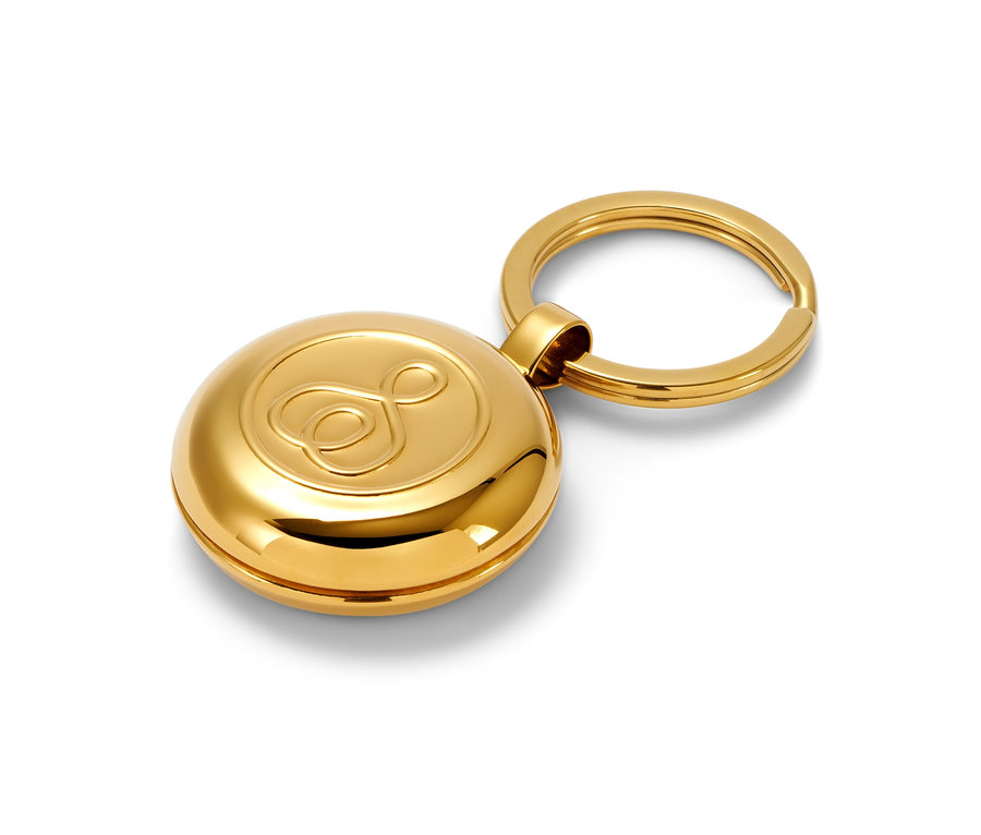 Zlaté pouzdro na léky s přívěskem na klíče na bílém pozadí.