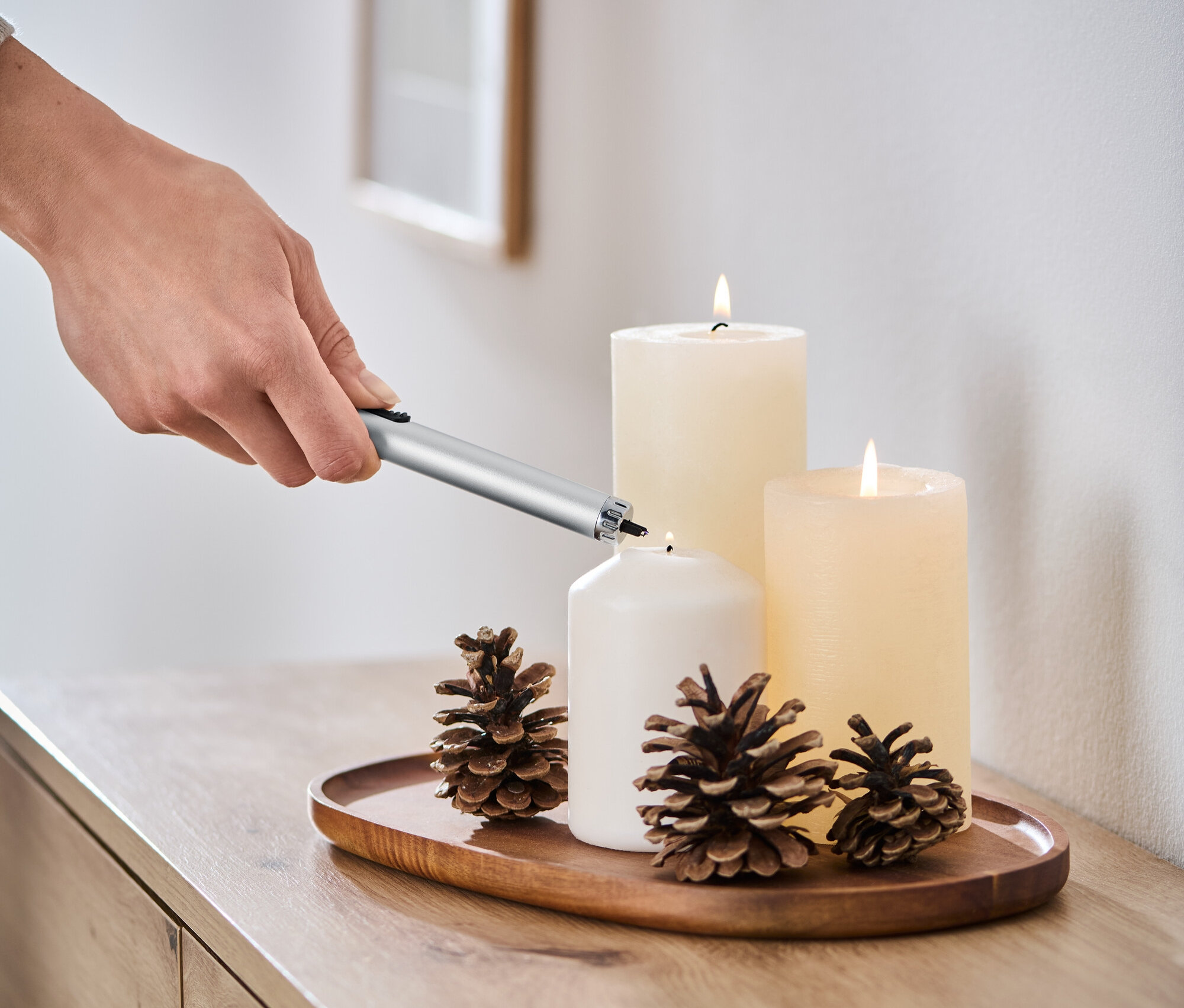 Ruka zapaluje bílou svíčku pomocí elektrického obloukového zapalovače.