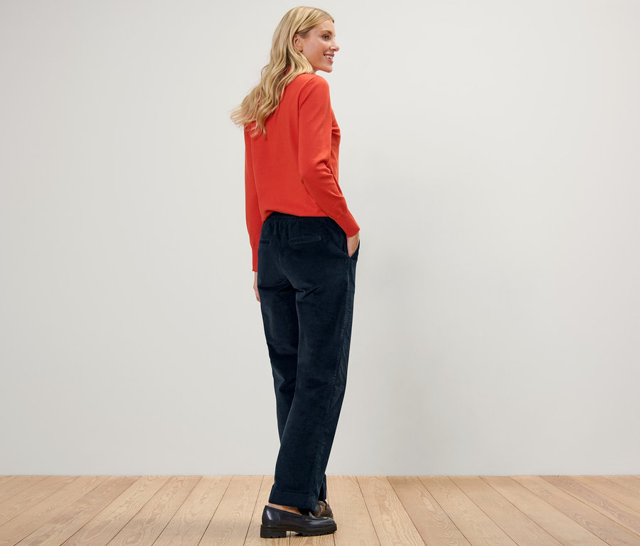 Žena pózuje v manšestrových kalhotách joggpant a oranžovém svetru.