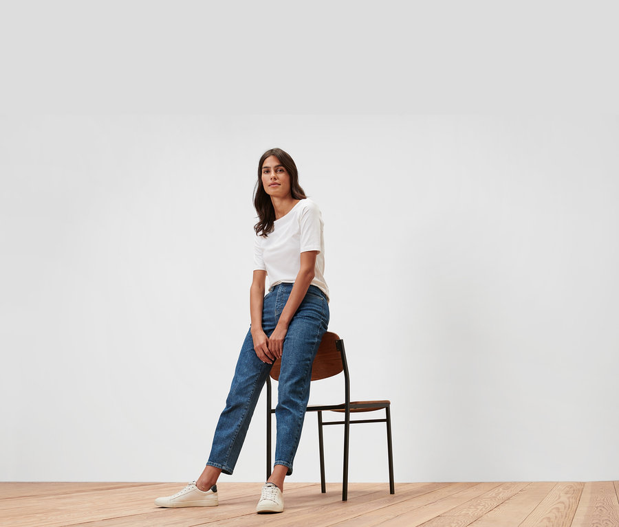 Žena sedí na židli v džínách mom – Fit »Nyla« a bílém tričku.