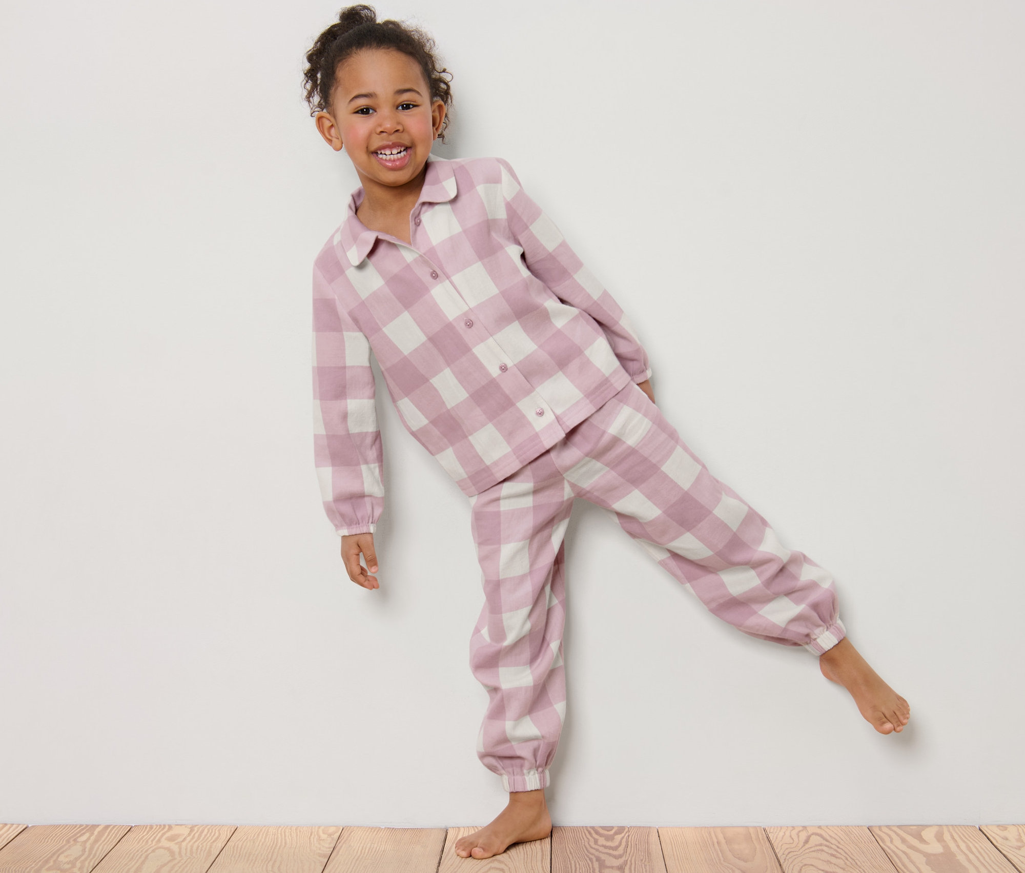 Usmívající se holčička pózuje v dětském flanelovém pyžamu s kostkovaným vzorem.