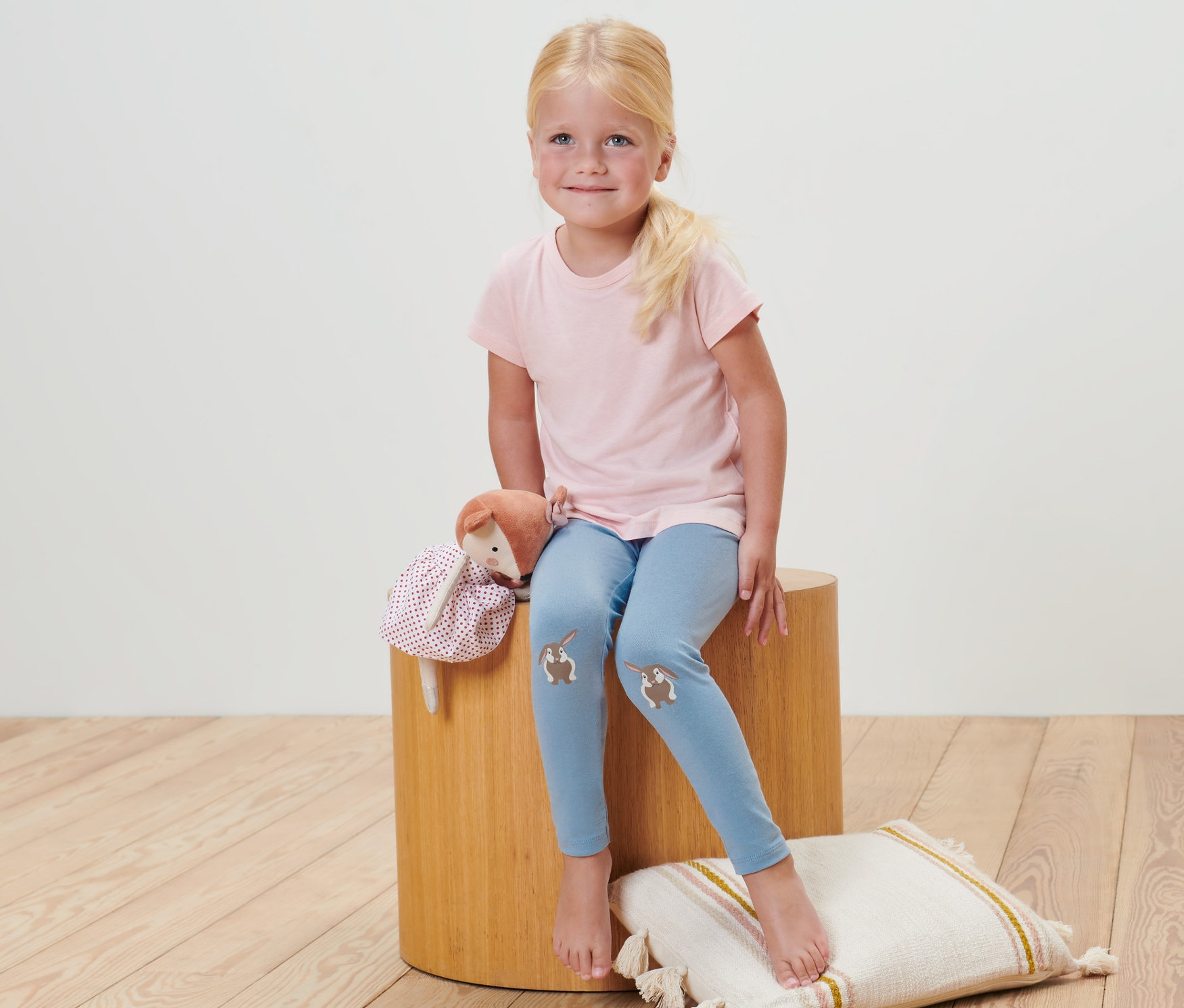 Dívka sedí na stoličce a má na sobě dětské legíny (2 ks, pruhy).