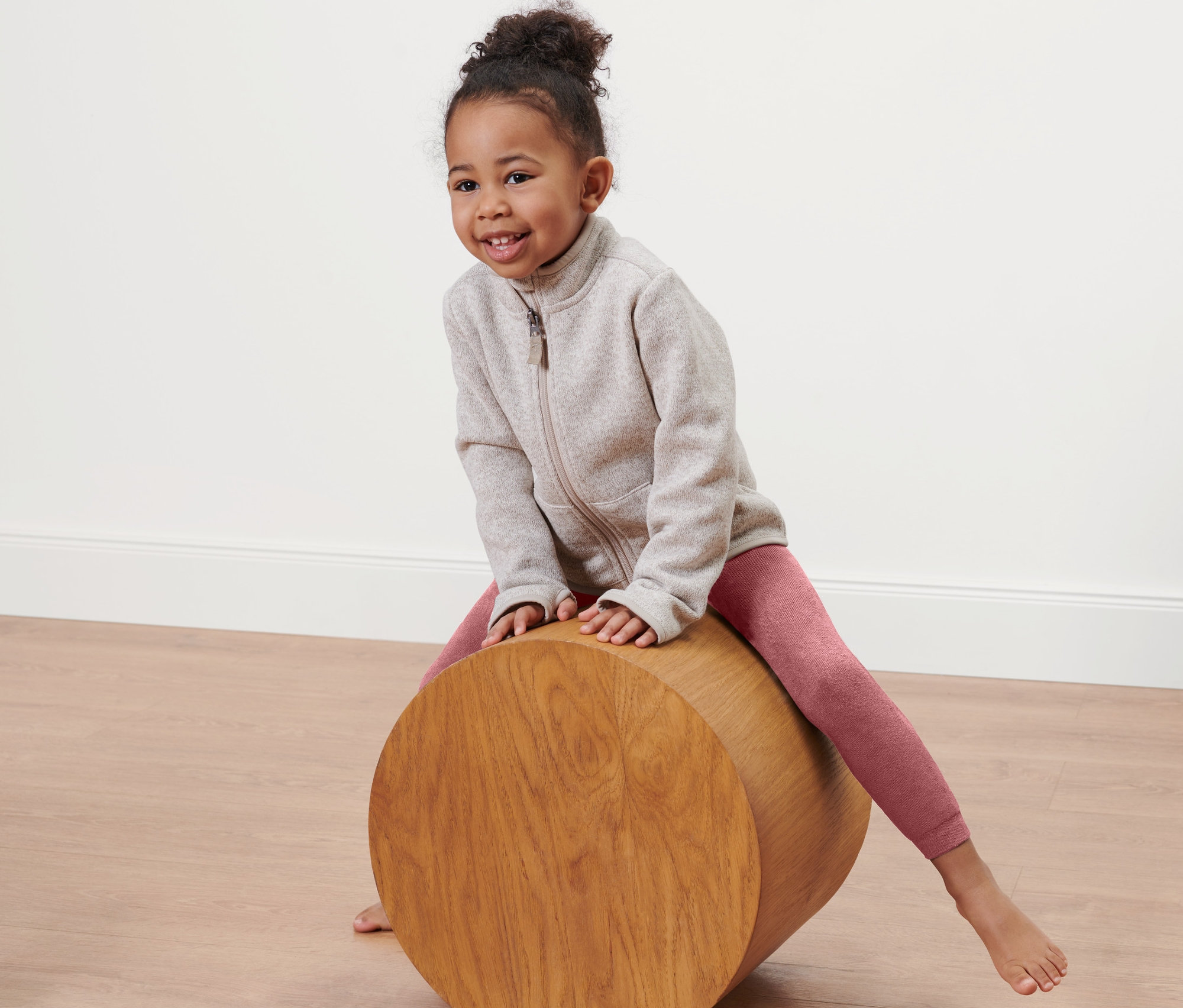 Dívka sedí na dřevěném válci a má na sobě růžové termolegíny.