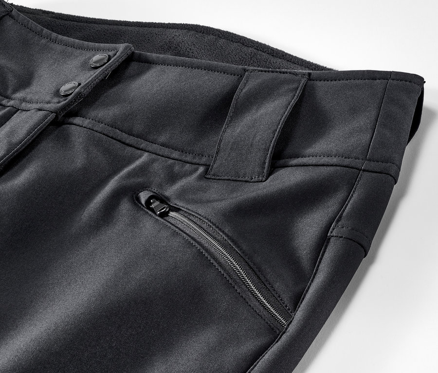 Detail lyžařských kalhot. Černé kalhoty mají zapínání na knoflíky a kapsu na zip.