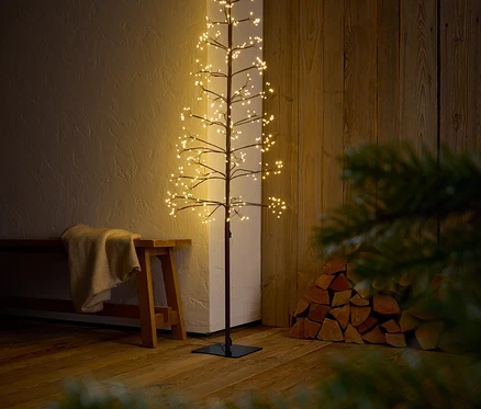 Dekorativní strom s větvemi a LED světly stojí v interiéru.
