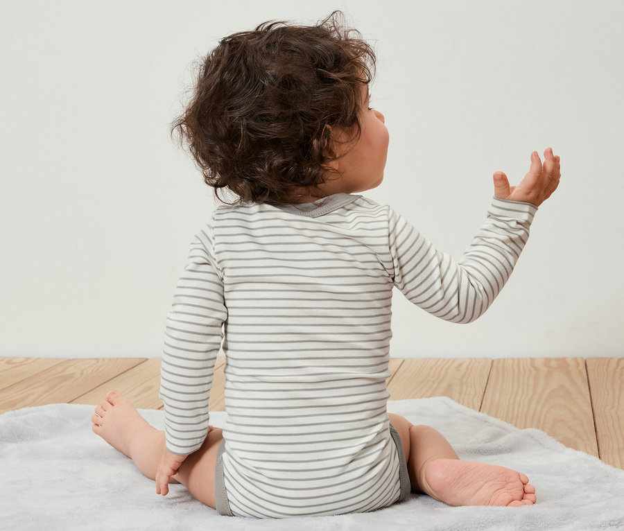 Dítě sedí zády k divákovi na podložce a má na sobě rostoucí body pro miminka, 5 ks.