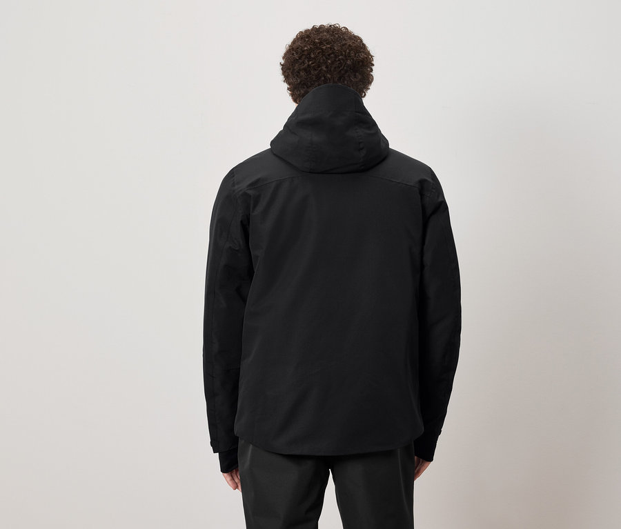 Muž s kudrnatými vlasy stojí zády a má na sobě černou bundu s kapucí.