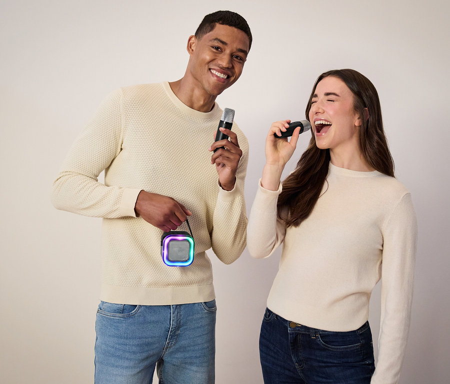 Muž drží mikrofon a reproduktor, žena zpívá do mikrofonu.