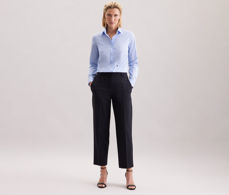 Žena ve světle modré halence Seidensticker Slim Fit non iron a tmavých kalhotách.