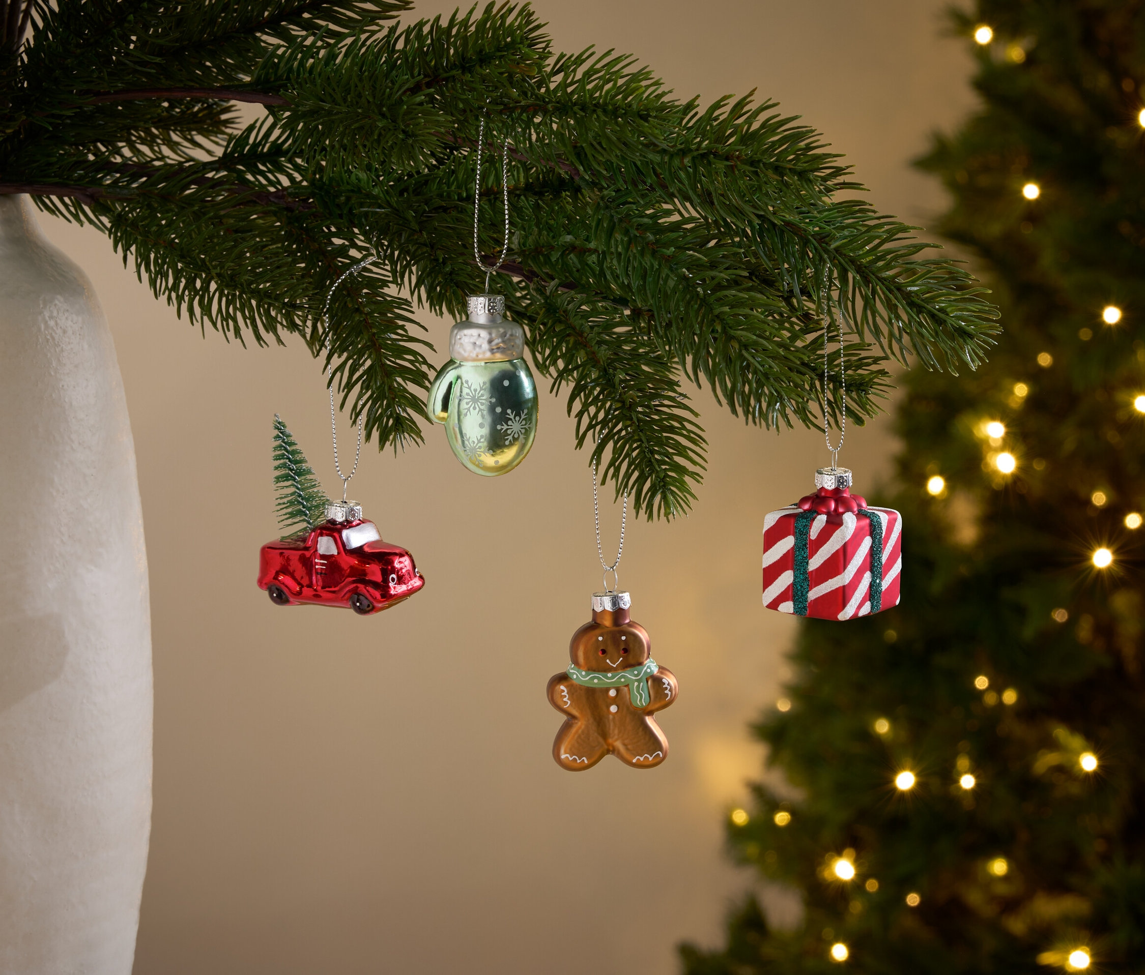 Větve vánočního stromku s ozdobami ve tvaru červeného auta s vánočním stromkem, rukavice, perníkového muže a dárku.