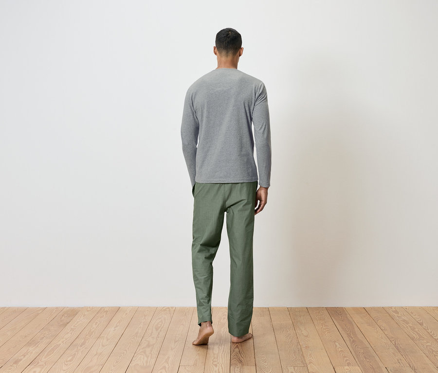 Muž zády k fotoaparátu má na sobě šedé tričko s dlouhým rukávem a zelené kalhoty.