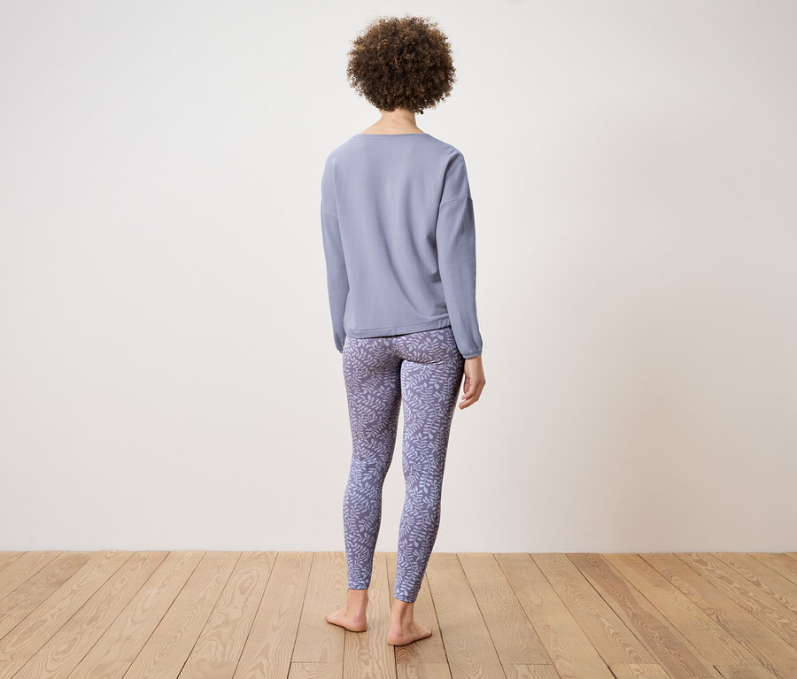 Žena zády k fotoaparátu má na sobě modrý top s dlouhým rukávem a vzorované legíny.