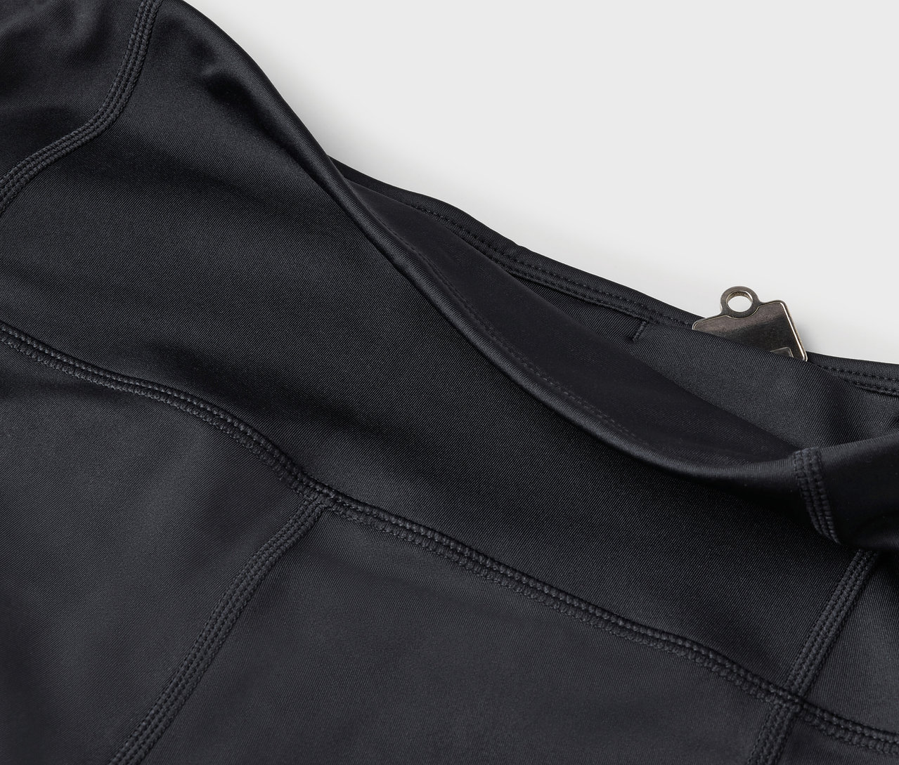 Detail černých legín s kapsou a stříbrným klipem.