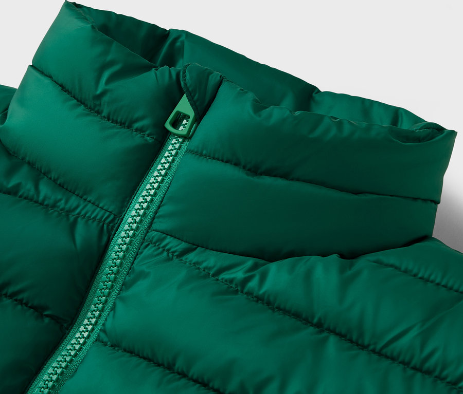 Detail zelené prošívané bundy s límcem a zipem.