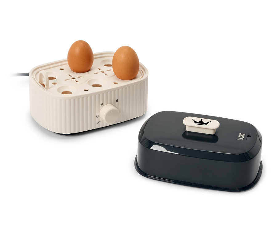 Dvě hnědá vejce na krémovém elektrickém vařiči vajec vedle černého víka.