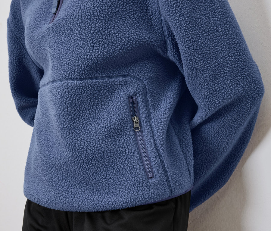 Detail modré fleecové mikiny s kapsou na zip.