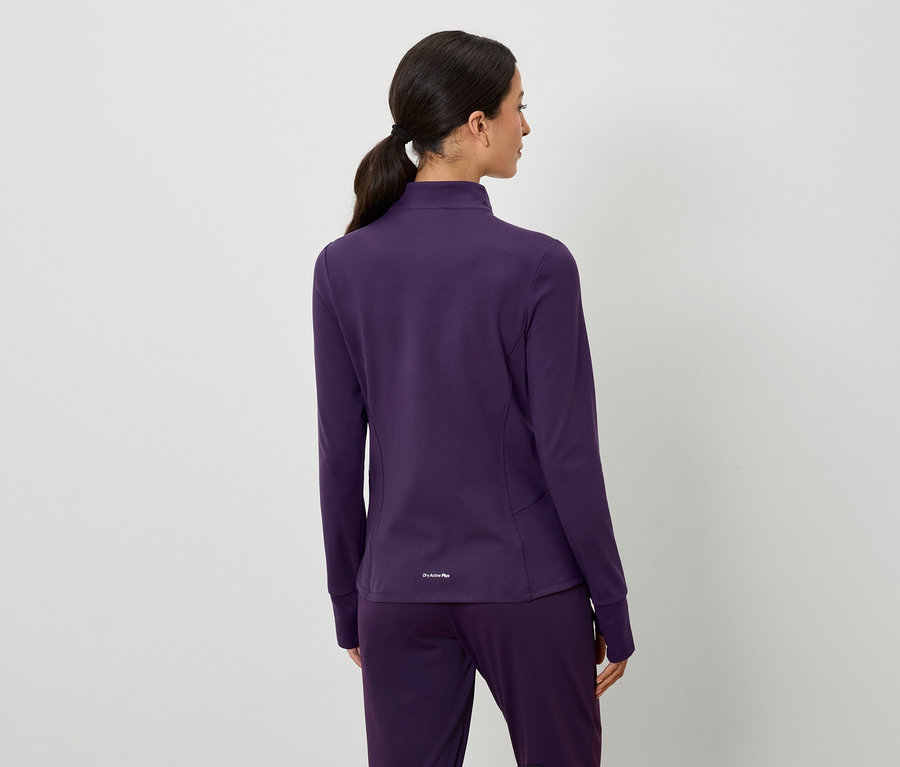 Zezadu pohled na ženu s hnědými vlasy staženými do culíku, oblečenou do fialové bundy a kalhot.