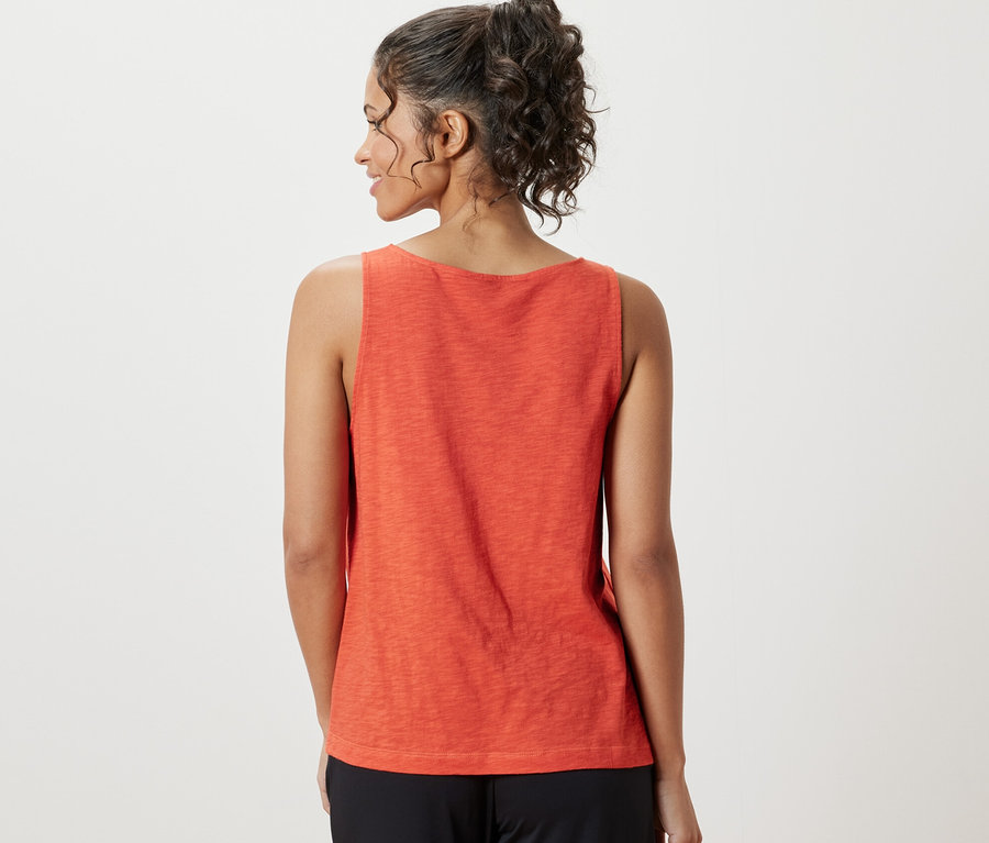 Žena má na sobě oranžový top z modalové směsi a černé kalhoty.