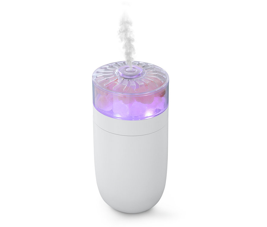 Bílý zvlhčovač vzduchu s růžovými krystaly soli a párou vycházející z horní části.