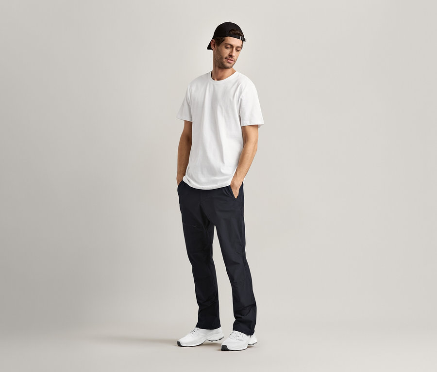 Muž stojí s rukama v kapsách a má na sobě 2 trička s kulatým výstřihem, bílá.