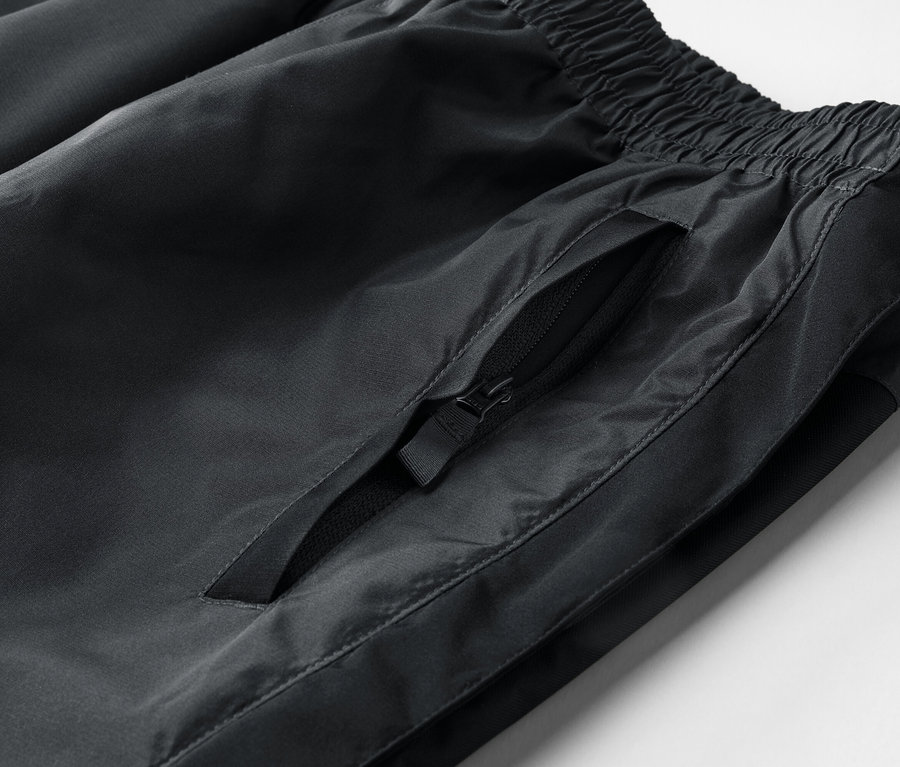 Detail černých tepláků s elastickým pasem a kapsou na zip.