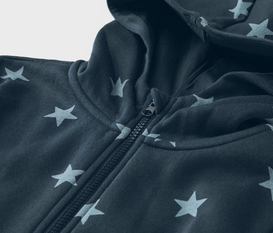 Detailní záběr na tmavě modrou mikinu s kapucí se vzorem hvězd a zipem.