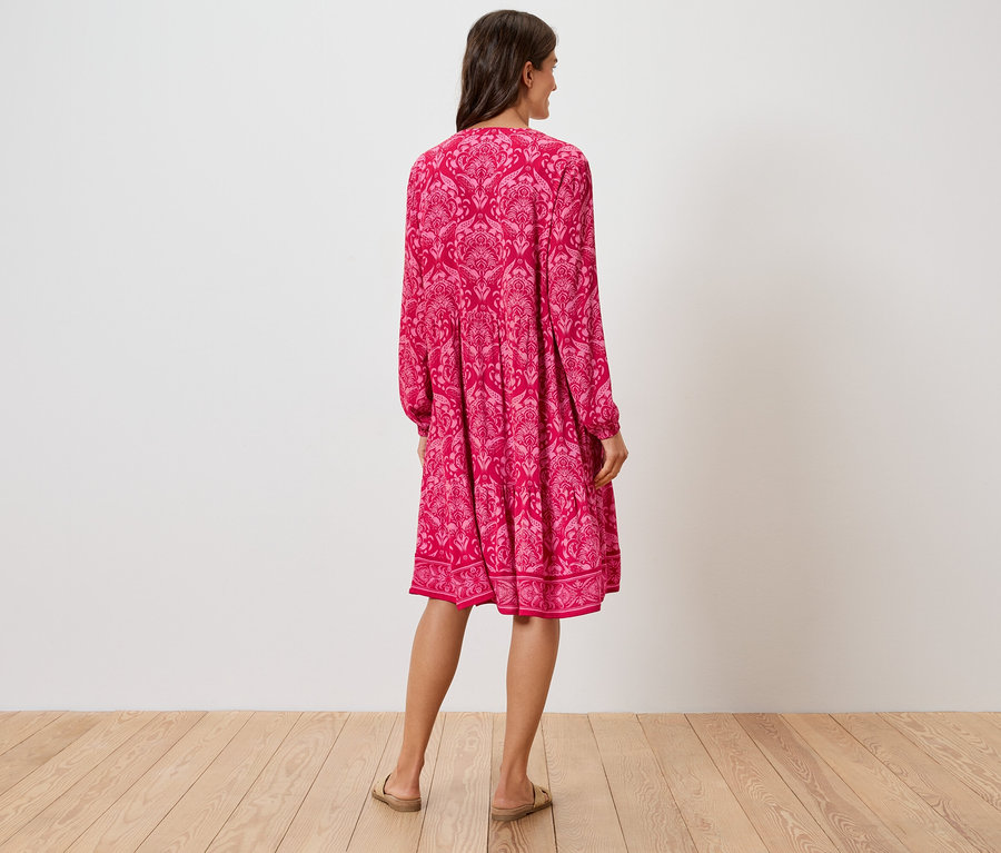 Pohled zezadu na ženu v růžových šatech ke kolenům s květinovým vzorem a sandálech.