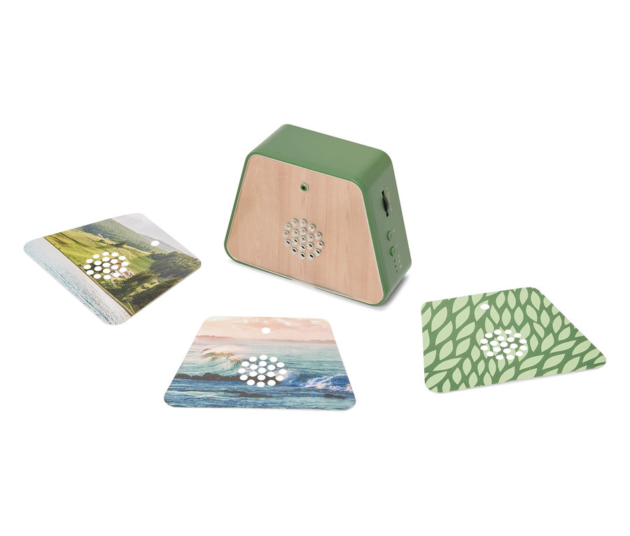 Zelený reproduktor s dřevěnými akcenty stojí na bílém povrchu, obklopený třemi čtvercovými kartami s motivy krajiny.