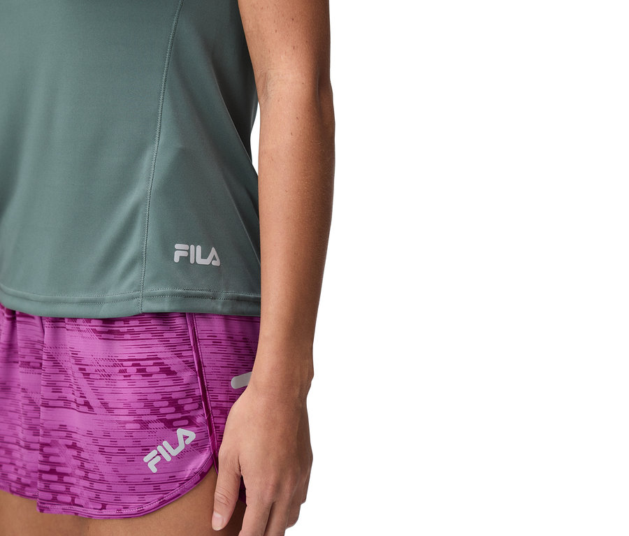 Detail ženy v zeleném topu Fila a fialových šortkách.